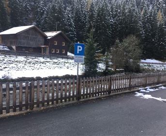 A winter landscape with a parking sign. In the background, traditional wooden houses and snowy trees can be seen.