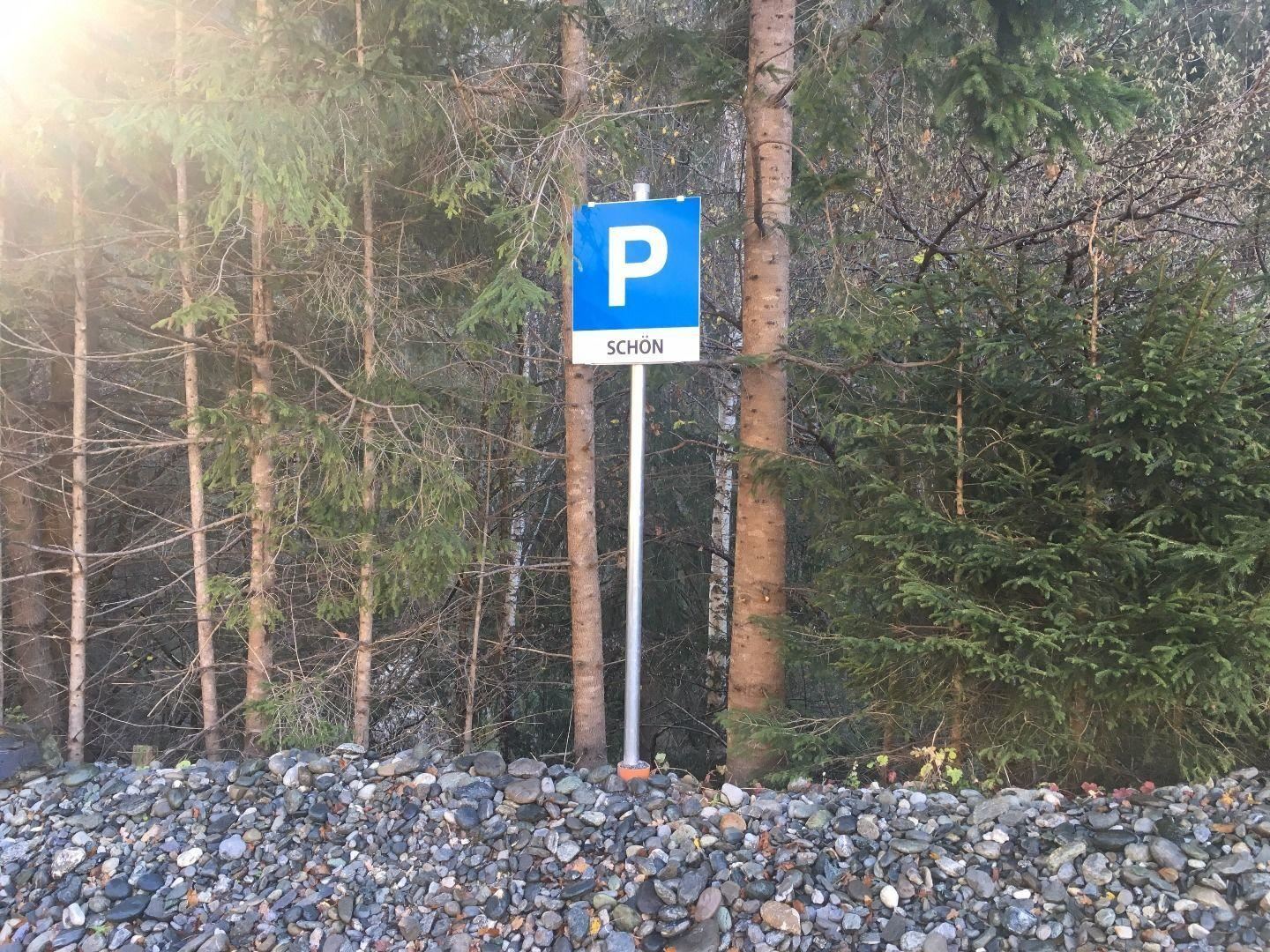 A parking sign stands between trees. The inscription on the sign says "BEAUTIFUL".