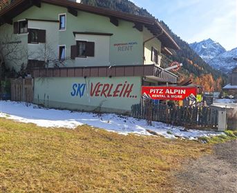 Ein Gebäude in den Bergen mit einem großen Schild für einen Skiverleih. Im Vordergrund liegt eine schneebedeckte Wiese.