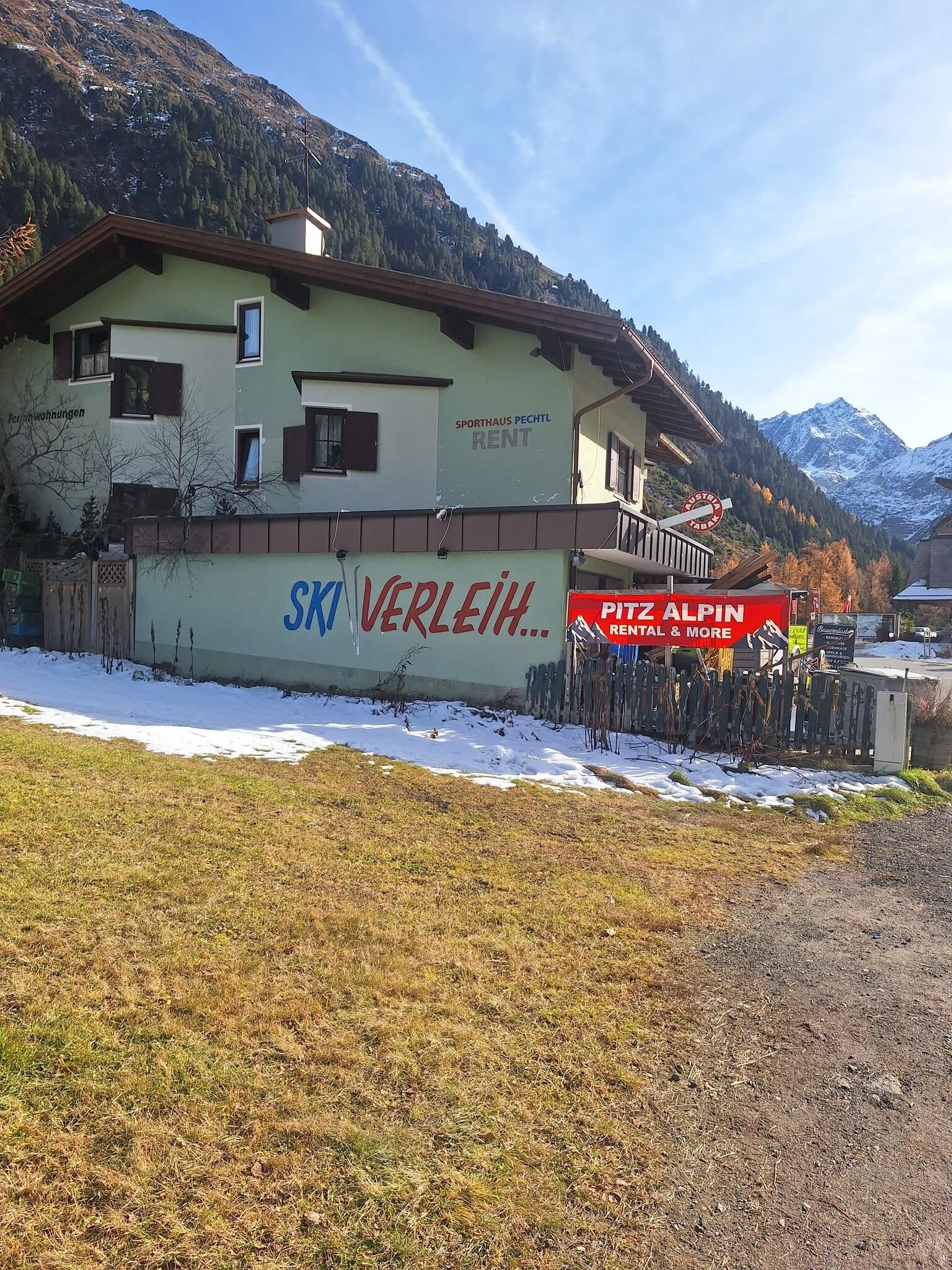 Ein Gebäude in den Bergen mit einem großen Schild für einen Skiverleih. Im Vordergrund liegt eine schneebedeckte Wiese.