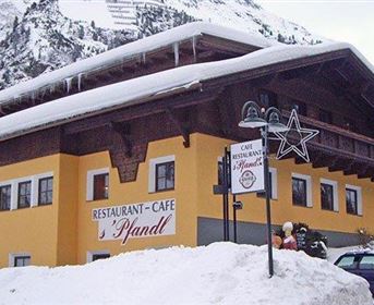 Ein gemütliches Restaurant-Café in den Bergen, umgeben von Schnee. Die Fassade ist gelb, mit einem traditionellen Alpenstil und vielen Fenstern.