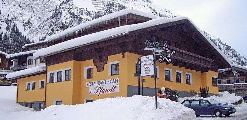 Ein gemütliches Restaurant-Café in den Bergen, umgeben von Schnee. Die Fassade ist gelb, mit einem traditionellen Alpenstil und vielen Fenstern.