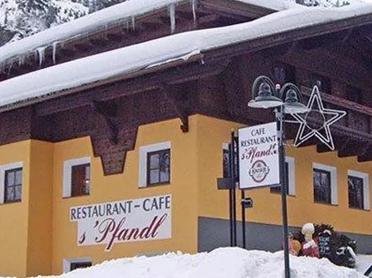 Ein gemütliches Restaurant-Café in den Bergen, umgeben von Schnee. Die Fassade ist gelb, mit einem traditionellen Alpenstil und vielen Fenstern.