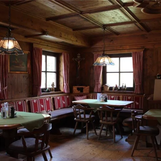 Ein traditioneller Gastraum mit Holzvertäfelung und gemütlichen Tischen. Die Fenster lassen viel Tageslicht herein und schaffen eine einladende Atmosphäre.