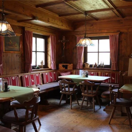 Ein rustikales Restaurant mit Holzwänden und gemütlichen Tischen. Die Fenster sind mit roten Vorhängen geschmückt und es gibt warme Lampen, die den Raum beleuchten.