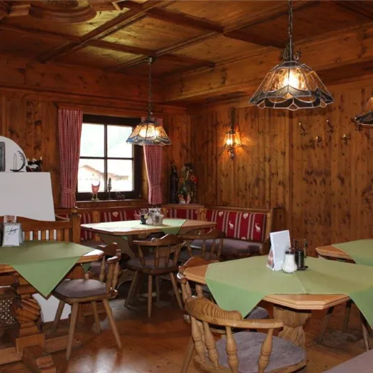 Ein gemütliches Restaurant mit holzvertäfelten Wänden und rustikalen Tischen. Die Tische sind mit grünen Tischdecken gedeckt und es gibt eine warme, einladende Atmosphäre.