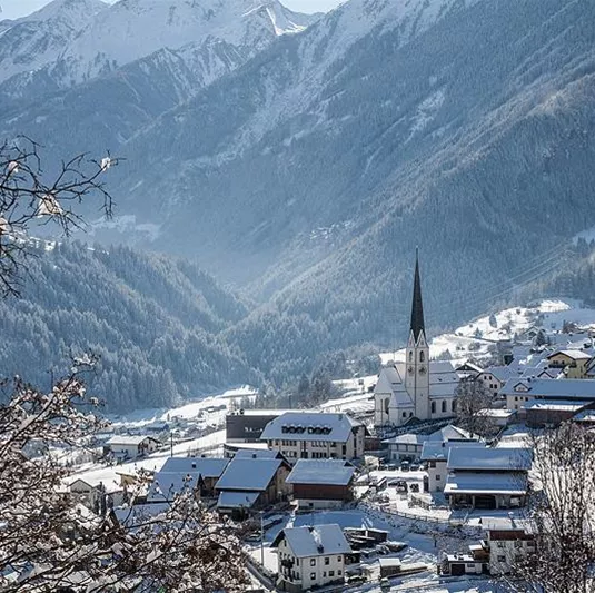Ein malerisches Dorf im Winter mit schneebedeckten Dächern und einer Kirche. Im Hintergrund erheben sich majestätische Berge.