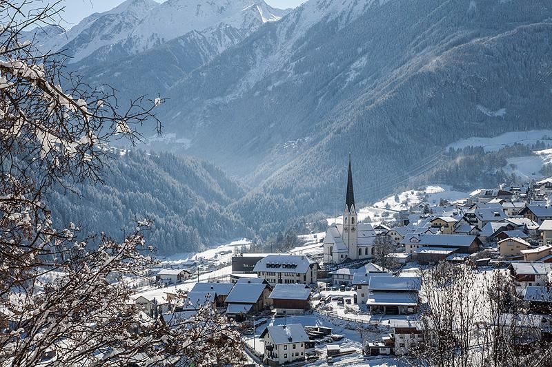 Ein malerisches Dorf im Winter mit schneebedeckten Dächern und einer Kirche. Im Hintergrund erheben sich majestätische Berge.