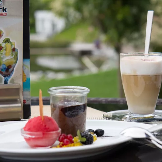 A dessert plate with a red sorbet, a chocolate pudding in a glass, and fresh berries. Next to it is a glass with a coffee milk drink.