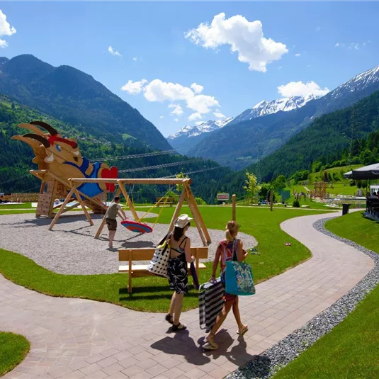 Ein schöner Spielplatz in der Natur mit Blick auf Berge und grünes Tal. Kinder spielen und genießen die frische Luft.
