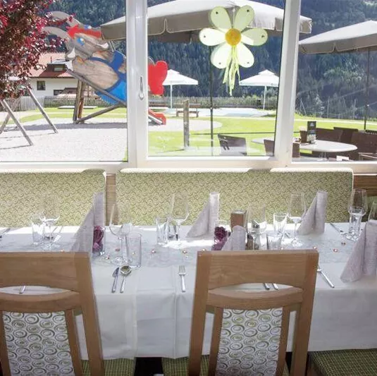 A cozy restaurant with a beautifully set table. In the background, you can see a playground and sun umbrellas.