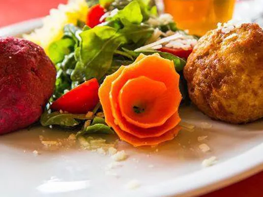 A beautiful plate with colorful balls and a fresh salad. The garnish of carrot flowers provides an attractive presentation.