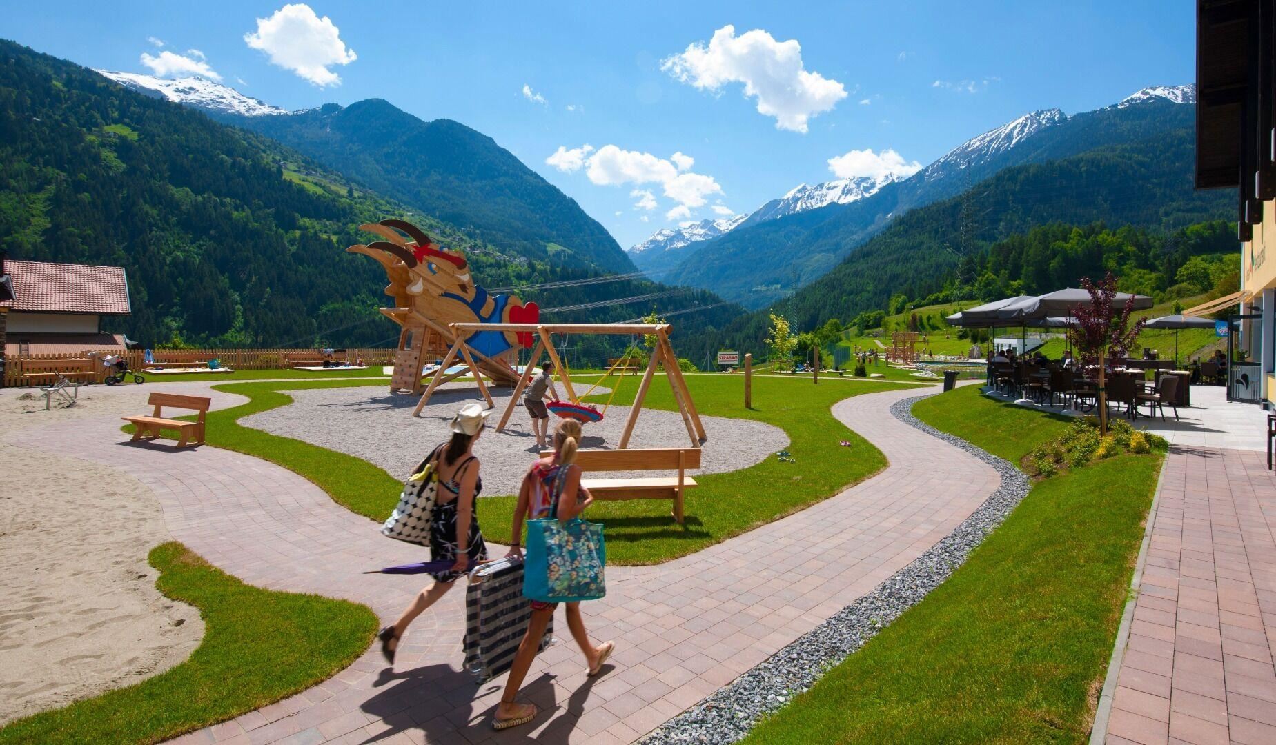 A beautiful playground with mountains in the background. Two women are walking on a path carrying shopping bags.