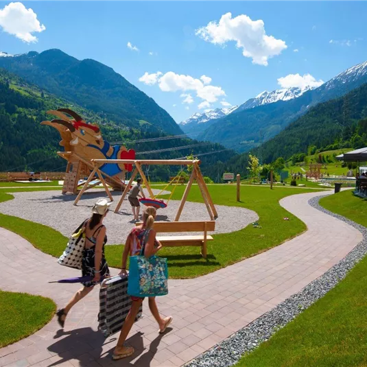 A beautiful playground with mountains in the background. Two women are walking on a path carrying shopping bags.