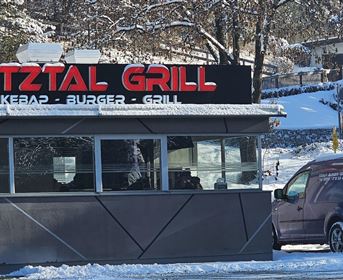 Ein kleines Restaurant mit dem Namen "Pizzería Grill". Es hat eine überdachte Terrasse und befindet sich in einer ruhigen Umgebung mit Bäumen.