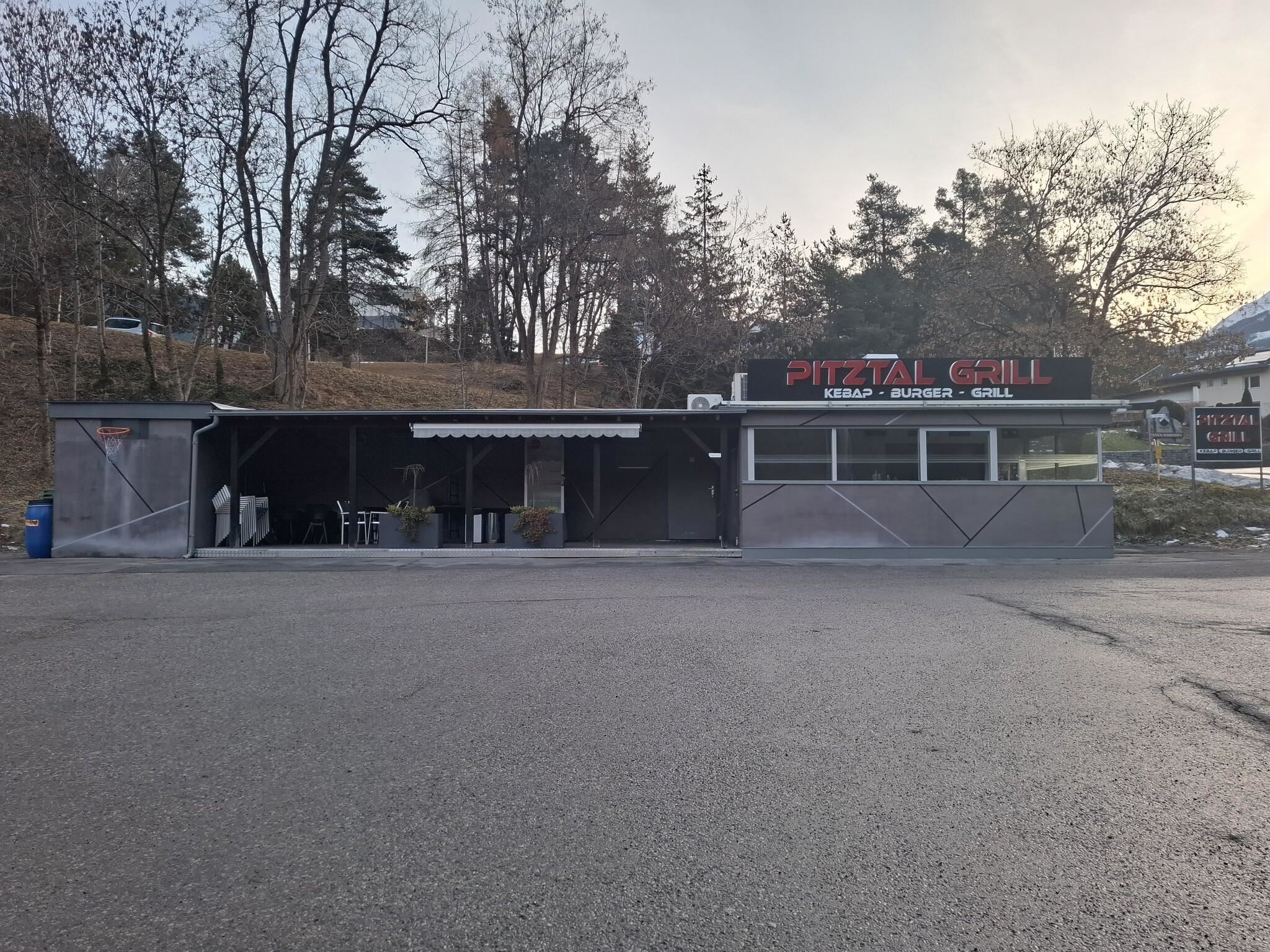 Ein kleines Restaurant mit dem Namen "Pizzería Grill". Es hat eine überdachte Terrasse und befindet sich in einer ruhigen Umgebung mit Bäumen.