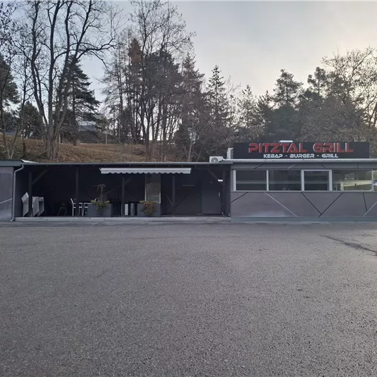 Ein kleines Restaurant mit dem Namen "Pizzería Grill". Es hat eine überdachte Terrasse und befindet sich in einer ruhigen Umgebung mit Bäumen.