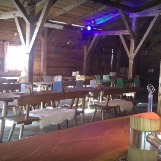 Ein rustikales Restaurant mit Holzdekor und langen Tischen. Der Bereich ist hell erleuchtet und schafft eine gemütliche Atmosphäre.
