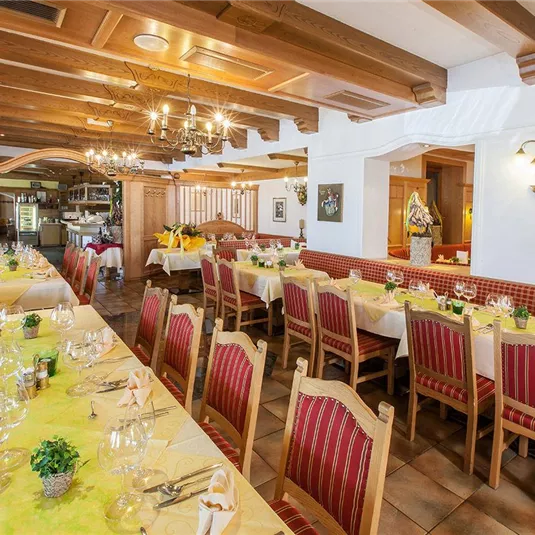 Ein gemütliches Restaurant mit langen Tischen und Holzdekor. Die Tischdecken sind gelb mit frischen Blumen als Dekoration, und die Atmosphäre wirkt einladend.