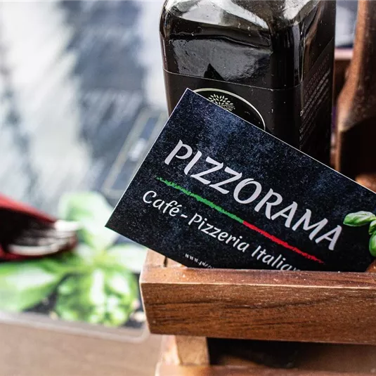 A placemat named "Pizzorama" for an Italian café and pizzeria. Also visible are a bottle of oil and a spice shaker.