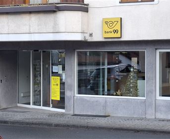 Eine Bankfiliale mit klaren Fenstern und einem auffälligen gelben Schild. Im Hintergrund ist ein Weihnachtsbaum sichtbar.