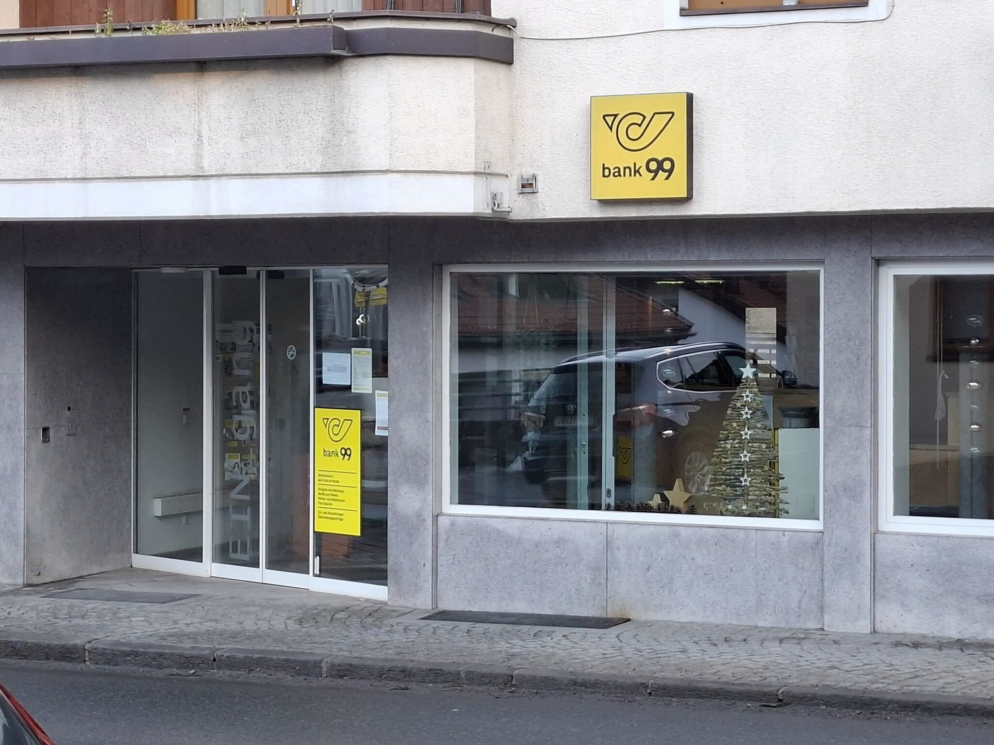 Eine Bankfiliale mit klaren Fenstern und einem auffälligen gelben Schild. Im Hintergrund ist ein Weihnachtsbaum sichtbar.