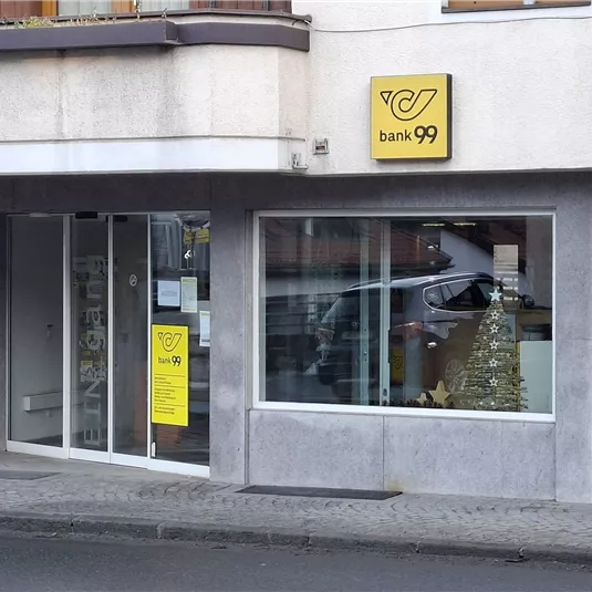 Eine Bankfiliale mit klaren Fenstern und einem auffälligen gelben Schild. Im Hintergrund ist ein Weihnachtsbaum sichtbar.