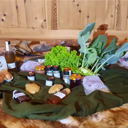 Eine rustikale Anordnung von frischen Lebensmitteln, darunter Gemüse, Eier und verschiedene Gläser mit Lebensmitteln. Ein kleines Schwein und ein Huhn sind ebenfalls zu sehen, umgeben von einer gemütlichen Umgebung.