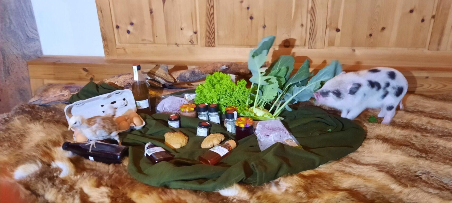 Eine rustikale Anordnung von frischen Lebensmitteln, darunter Gemüse, Eier und verschiedene Gläser mit Lebensmitteln. Ein kleines Schwein und ein Huhn sind ebenfalls zu sehen, umgeben von einer gemütlichen Umgebung.