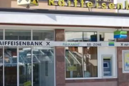 Die Raiffeisenbank mit großen Fenstern und einem klaren Entrée. Es gibt eine digitale Anzeigetafel und einen SB-Bereich vor dem Gebäude.