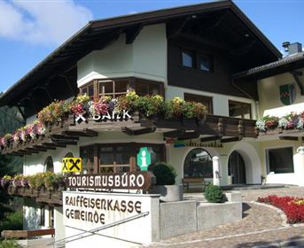 A charming mountain cabin with blooming flowers on the balcony. The building houses a tourism office and a bank.