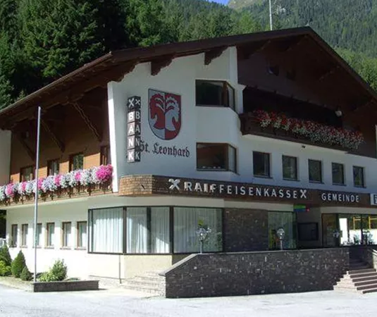 Ein traditionelles, mehrstöckiges Gebäude mit einem rustikalen Dach. Die Fassade ist mit bunten Blumen geschmückt und es umgeben hohe Bäume.