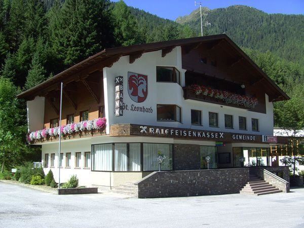 Ein traditionelles, mehrstöckiges Gebäude mit einem rustikalen Dach. Die Fassade ist mit bunten Blumen geschmückt und es umgeben hohe Bäume.