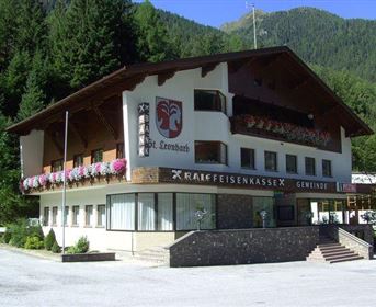 Ein gepflegtes Gebäude in den Bergen mit Blumenbalkonen. Umgeben von Bäumen und einer schönen Landschaft.