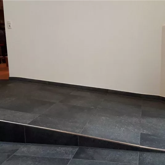 Ein moderner Eingangsbereich mit dunklem Fliesenboden. Der Raum hat eine helle Wand und eine leicht erhöhte Fläche.