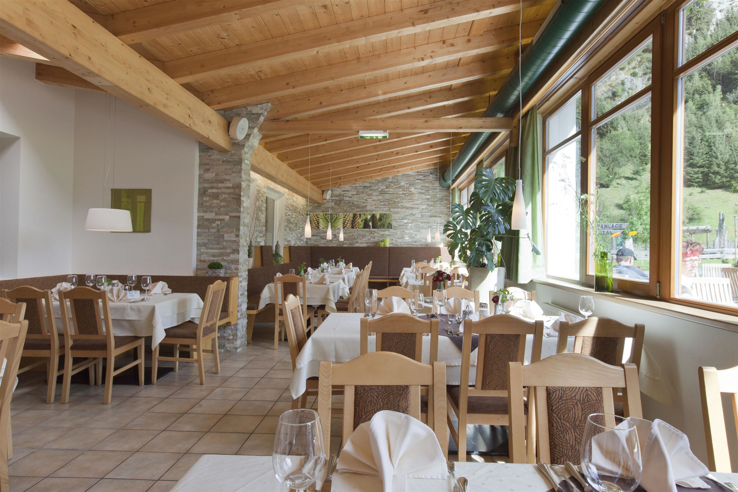 Ein einladendes Restaurant mit Holzbalkendecke und eleganten Tischen. Große Fenster bieten einen Blick auf die Natur draußen.