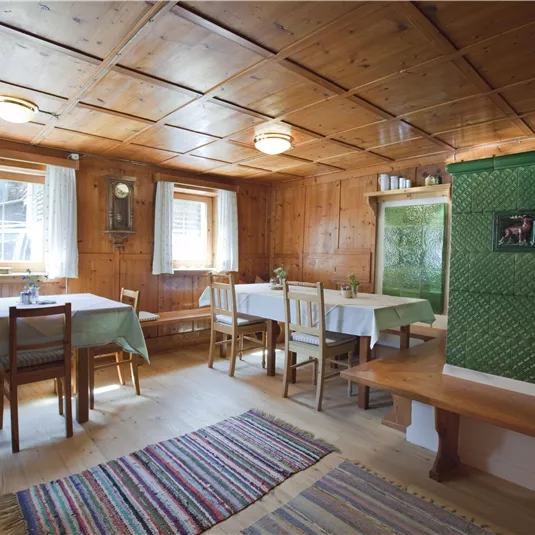 Ein gemütlicher Raum mit Holzwänden und Tischen. Ein traditioneller Ofen in der Ecke sorgt für eine einladende Atmosphäre.