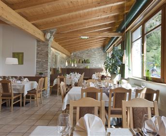 Ein einladendes Restaurant mit Holzbalkendecke und hellen Tischen. Große Fenster bieten einen Blick auf die Natur.