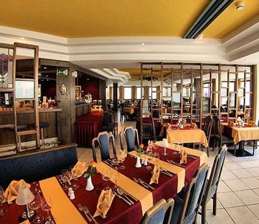 Ein gemütliches Restaurant mit eleganten Tischen und gelbem Akzent. Die Atmosphäre ist einladend und ideal für ein Essen mit Freunden oder Familie.