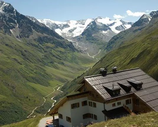 A picturesque valley with green meadows and majestic mountain peaks. In the foreground, there is a charming house.