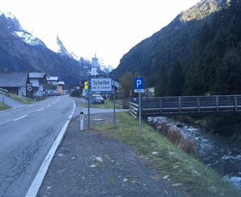 Ein malerisches Dorf in den Bergen mit einem Fluss und einer Brücke. Die Landschaft zeigt hohe Berge und eine ruhige Straße.
