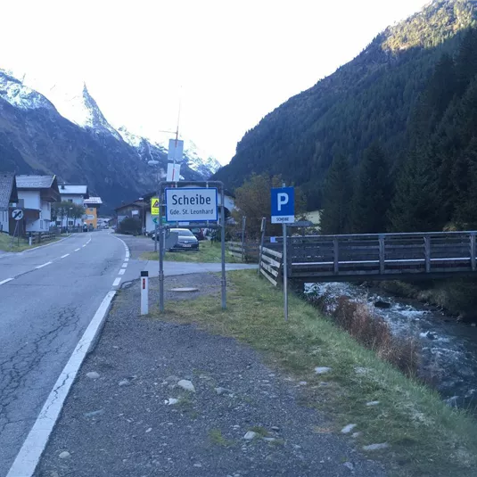 Ein malerisches Dorf in den Bergen mit einem Fluss und einer Brücke. Die Landschaft zeigt hohe Berge und eine ruhige Straße.