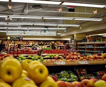 Ein buntes Obstregal in einem Supermarkt mit verschiedenen Apfelsorten und anderen Früchten. Kunden wählen frisches Obst aus.