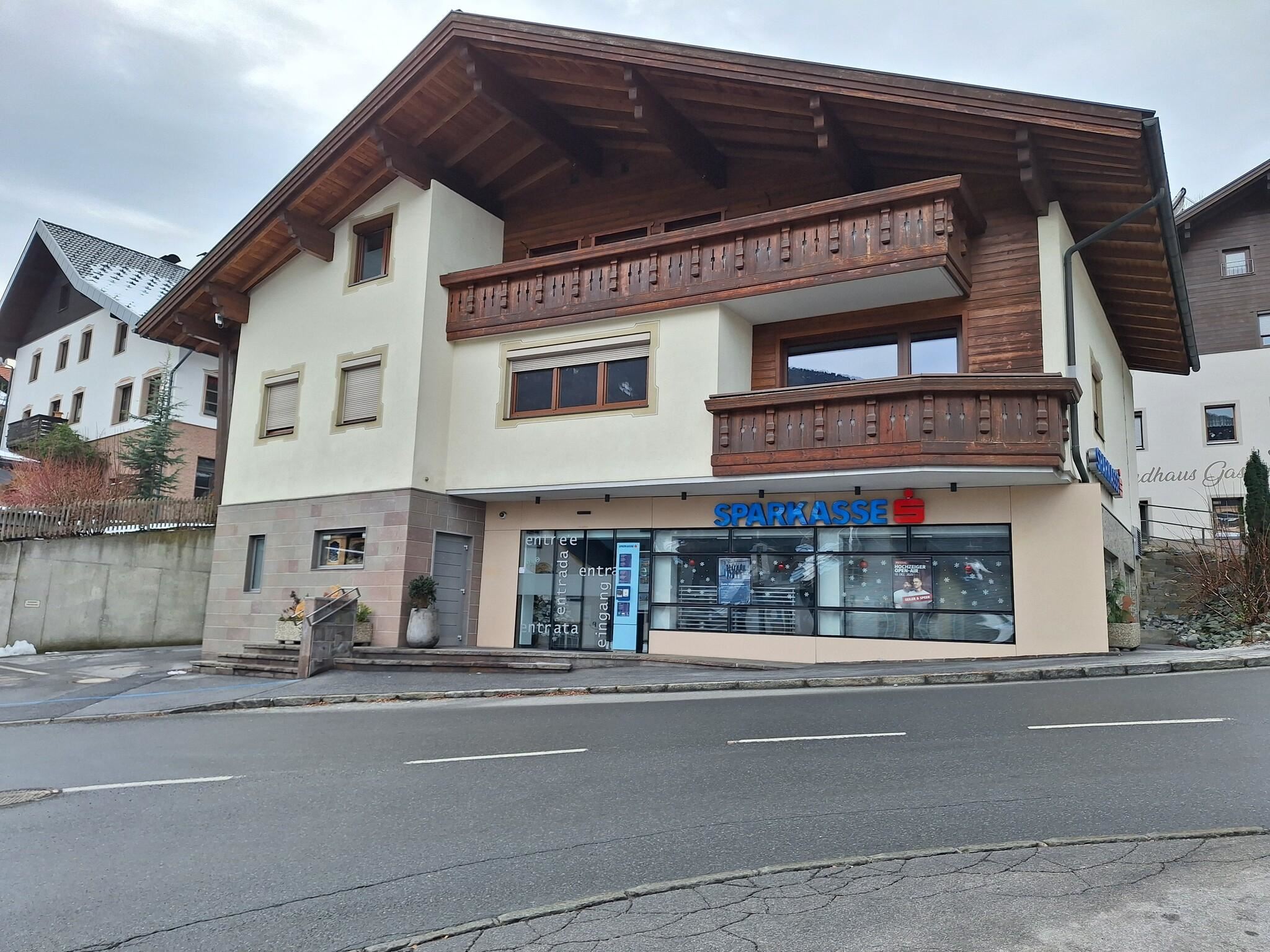 Ein modernes Gebäude mit Holzverkleidung und einem großen Fenster im Erdgeschoss. Es befindet sich an einer Straße und hat einen klaren Himmel im Hintergrund.