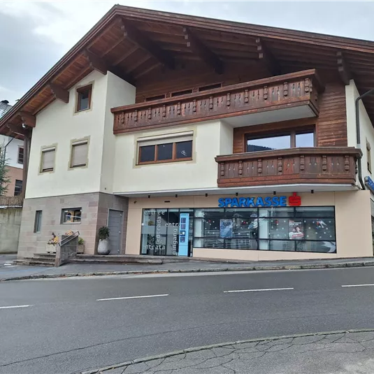 Ein modernes Gebäude mit Holzverkleidung und einem großen Fenster im Erdgeschoss. Es befindet sich an einer Straße und hat einen klaren Himmel im Hintergrund.