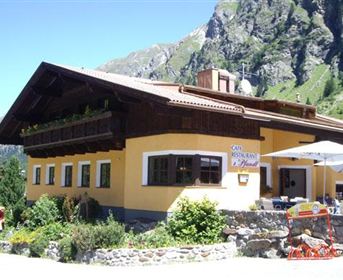 A cozy restaurant building with traditional architecture in the mountains. Surrounded by green plants and impressive rocks.