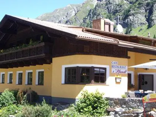 A cozy restaurant building with traditional architecture in the mountains. Surrounded by green plants and impressive rocks.
