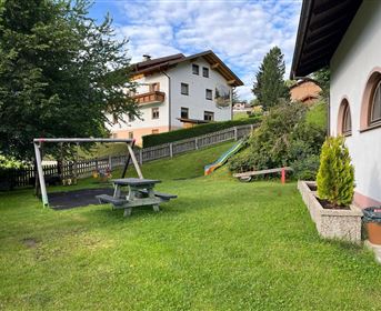 Ein gepflegter Garten mit einer Schaukel und einer Rutsche. Im Hintergrund sind ein paar Wohnhäuser und Bäume zu sehen.