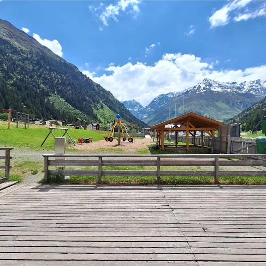 A beautiful playground in the mountains, surrounded by green meadows and tall mountains. The sky is clear and the sun is shining.