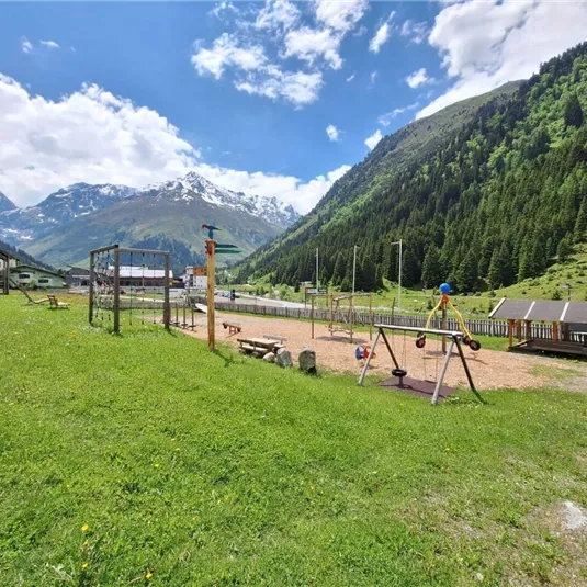 A beautiful playground in a green landscape, surrounded by mountains. The sky is blue with a few clouds.